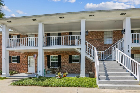 A two-story building with a covered porch, brick facade, and a staircase leading to the upper level.