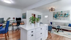 Een moderne woonkamer met een witte bank, een salontafel, een bureau met een computer en een groot abstract schilderij aan de muur.