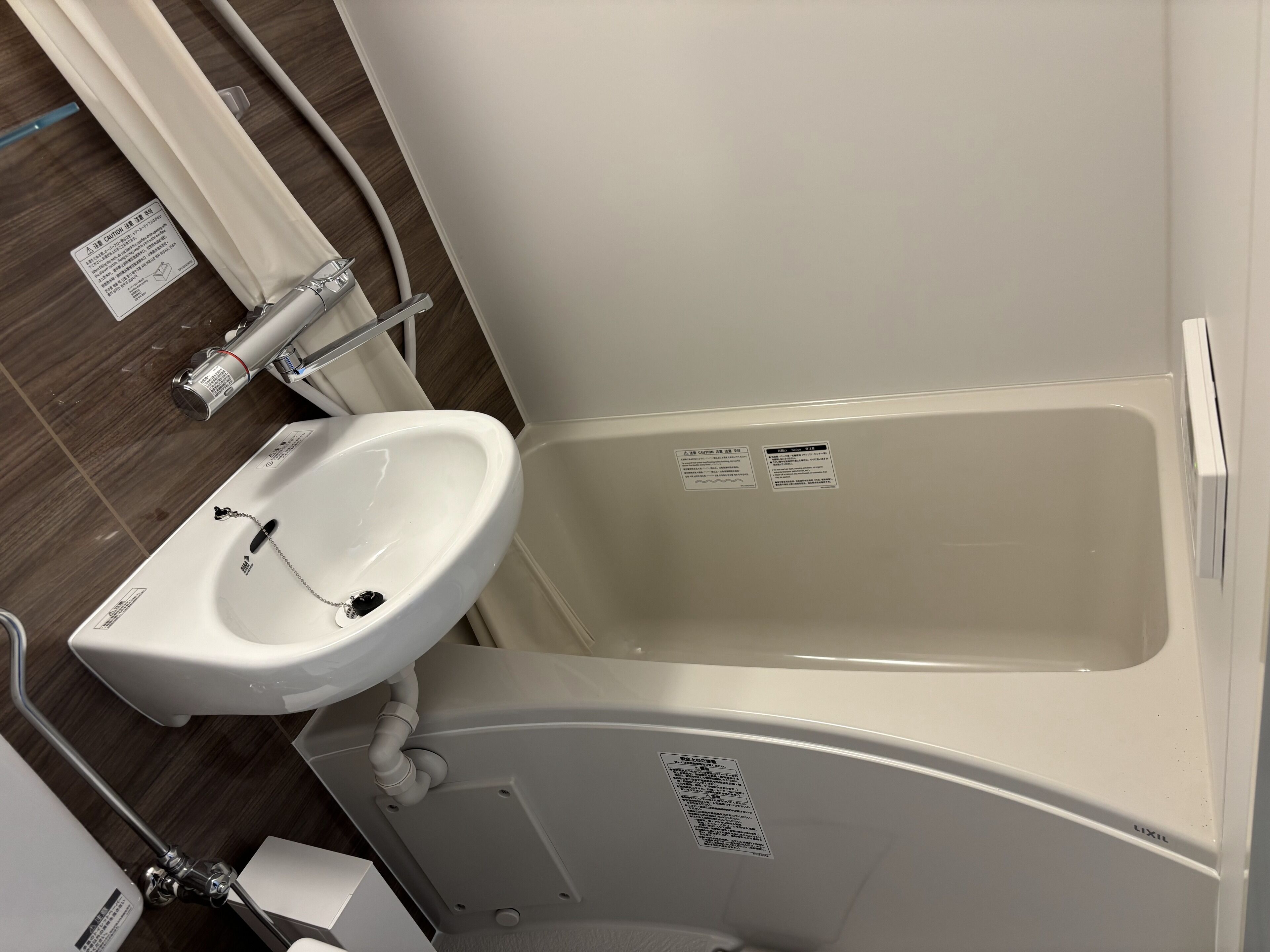 A bathroom with a white sink, a bathtub, and a toilet. There are warning labels on the bathtub and sink.