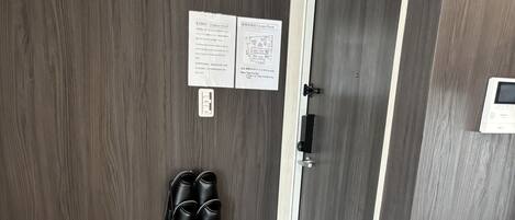 A room with a wooden wall, a door with a handle, a shoe rack, and a small mat at the entrance.