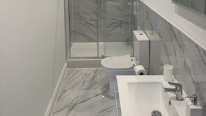 Ett modernt badrum med en dusch som är avskärmad med glasväggar, ett vitt handfat och en stor spegel.