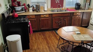 Une cuisine compacte équipée d’une cuisinière, d’un four à micro-ondes et d’un évier. On y trouve une table à manger avec des chaises et une poubelle.
