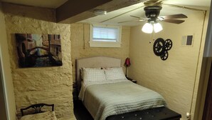 Une chambre à coucher comprenant un lit, un banc, un ventilateur de plafond, une fenêtre et un élément décoratif fixé au mur.