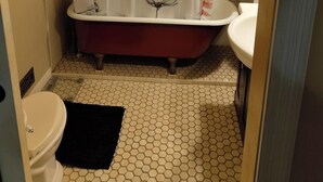 Une salle de bain avec une baignoire sur pieds rouge, des toilettes blanches et un lavabo blanc.