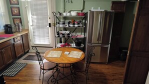 Une cuisine avec une table en bois, des chaises, un réfrigérateur en acier inoxydable et une étagère en métal.