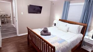 Een slaapkamer met een houten bed, een plafondventilator, een flatscreen-televisie en een raam met gordijnen.