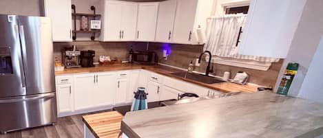 A modern kitchen with white cabinets, stainless steel appliances, and a wooden countertop.