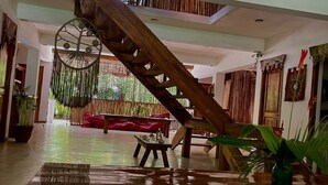 A spacious interior with a wooden staircase, a hanging chair, and a red sofa. - Ganesh Hostel (El Valle)