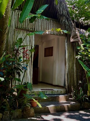 A rustic wooden structure with a thatched roof, surrounded by lush greenery and potted plants. - Ganesh Hostel (El Valle)