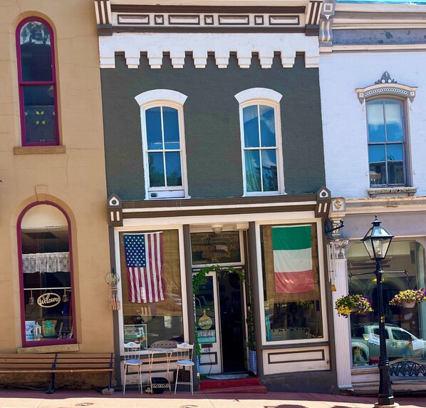 A storefront with two large windows, a welcoming sign, and a flag.