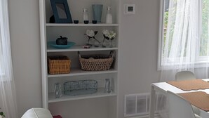Un salon moderne avec un canapé blanc, une table à manger blanche avec des chaises, une bibliothèque blanche et une fenêtre ornée de rideaux légers.
