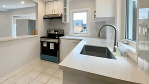 Une cuisine moderne avec des meubles blancs, une cuisinière noire et une grande fenêtre qui laisse entrer la lumière naturelle.