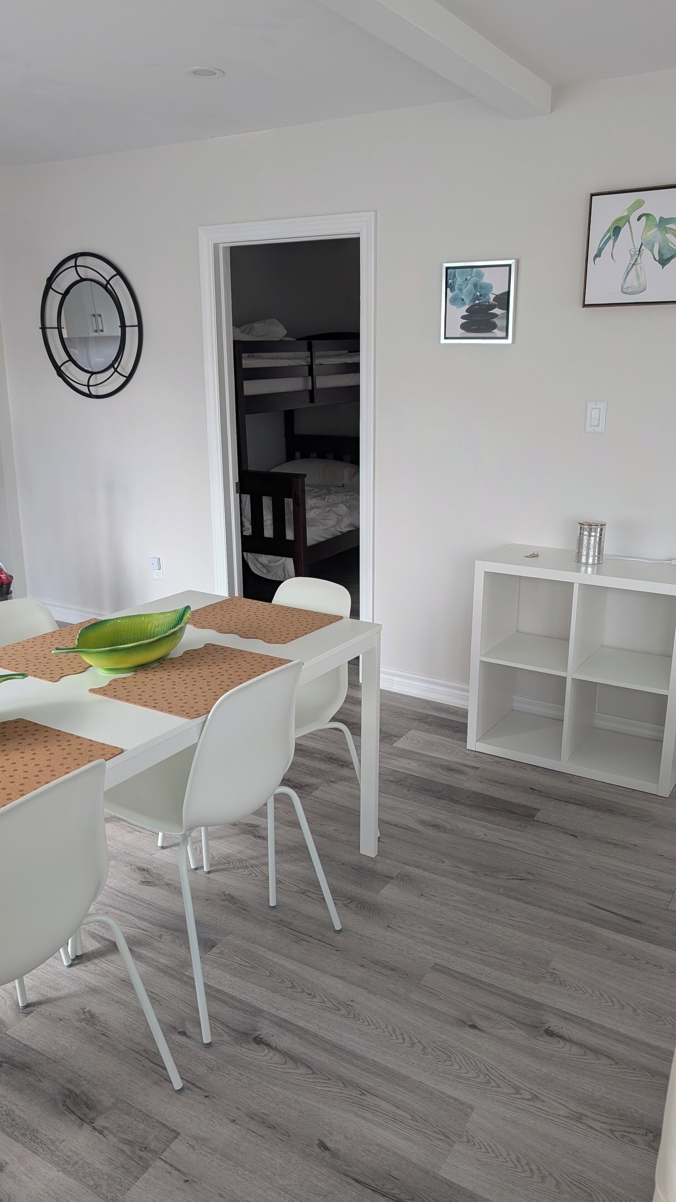 A modern room with a dining table, white chairs, a bunk bed, and a white shelving unit.
