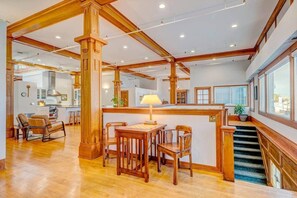 Un ambiente spazioso con travi in legno, un'area pranzo con tavolo e sedie, una cucina sullo sfondo e una scala che conduce a un livello superiore.