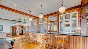 Zona de bar con taburetes de madera, una barra y vista a la cocina a través de una ventana.