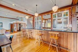 Angolo bar con sgabelli di legno, un bancone e vista sulla cucina attraverso una finestra.