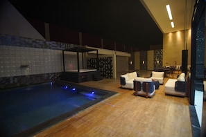 Un espace piscine intérieur moderne, doté d’un jacuzzi, de coins salon et d’un bar.