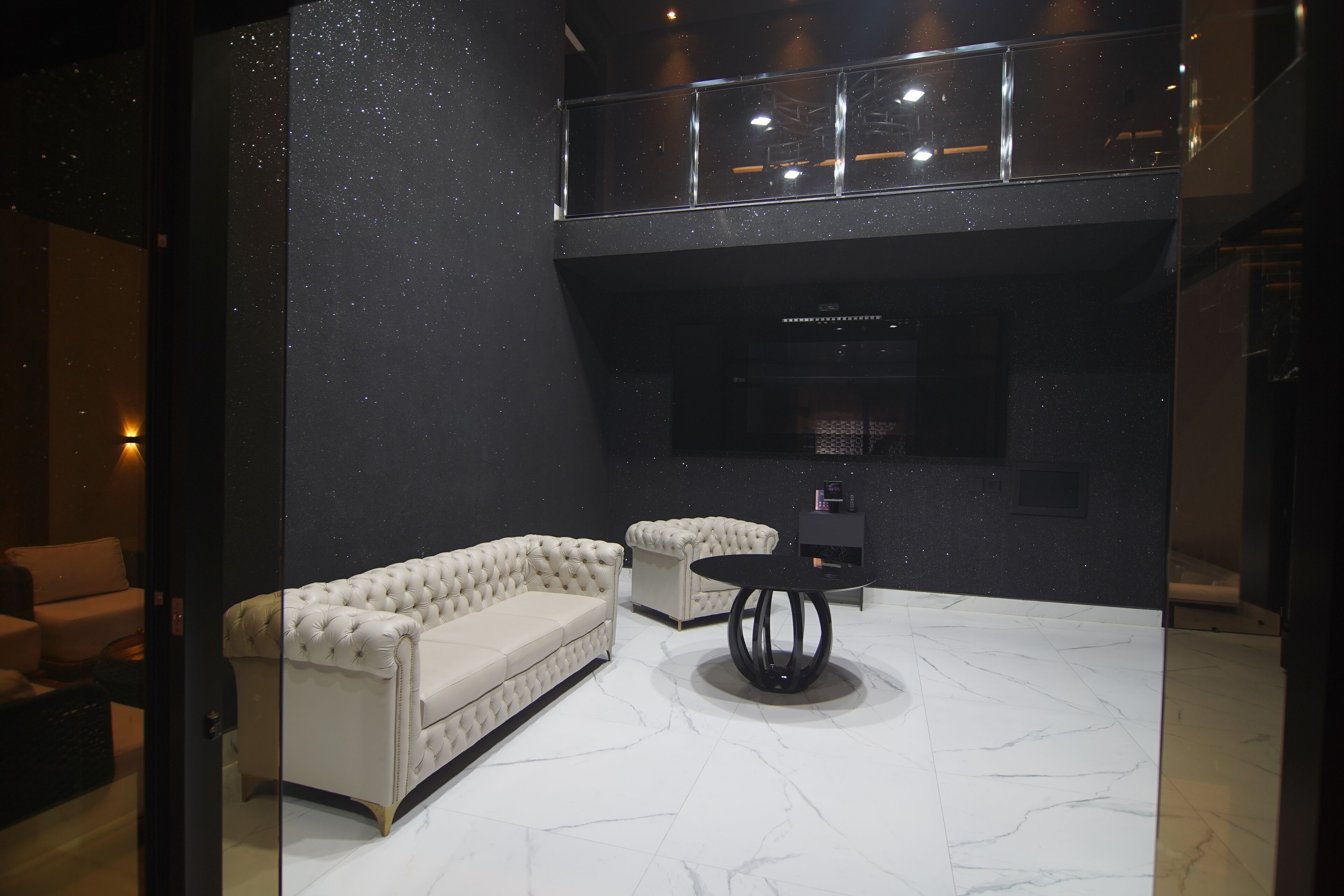 A modern interior with a tufted sofa, a round table, and a high ceiling with a balcony.