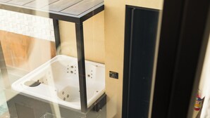 Un espacio moderno para comer al aire libre con una mesa redonda de madera y sillas azules con cojines, una bañera de hidromasaje y un porche con paredes de vidrio.