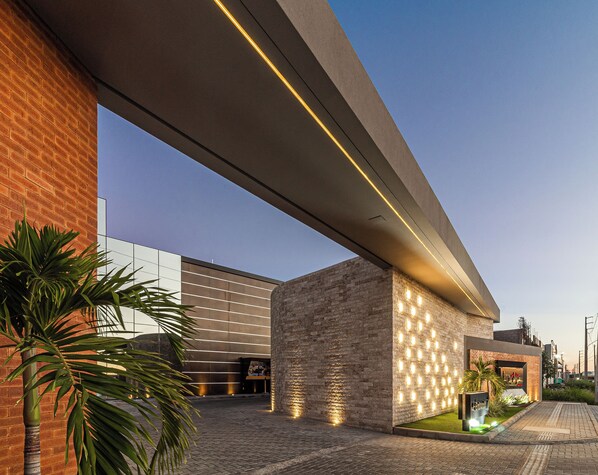 Un bâtiment moderne avec une façade en briques, un toit plat et un espace d’entrée pavé agrémenté de plantes.