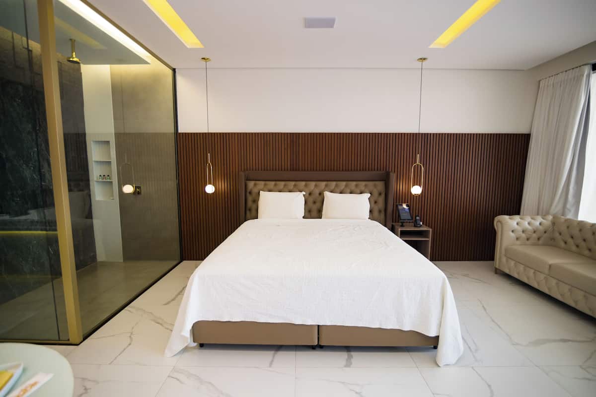 Une chambre moderne avec un grand lit, une douche à l’italienne en verre, un canapé et des luminaires suspendus.