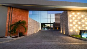 Una entrada moderna a un edificio con fachada de ladrillo, una estructura de vidrio al fondo y un sendero que conduce a la entrada.