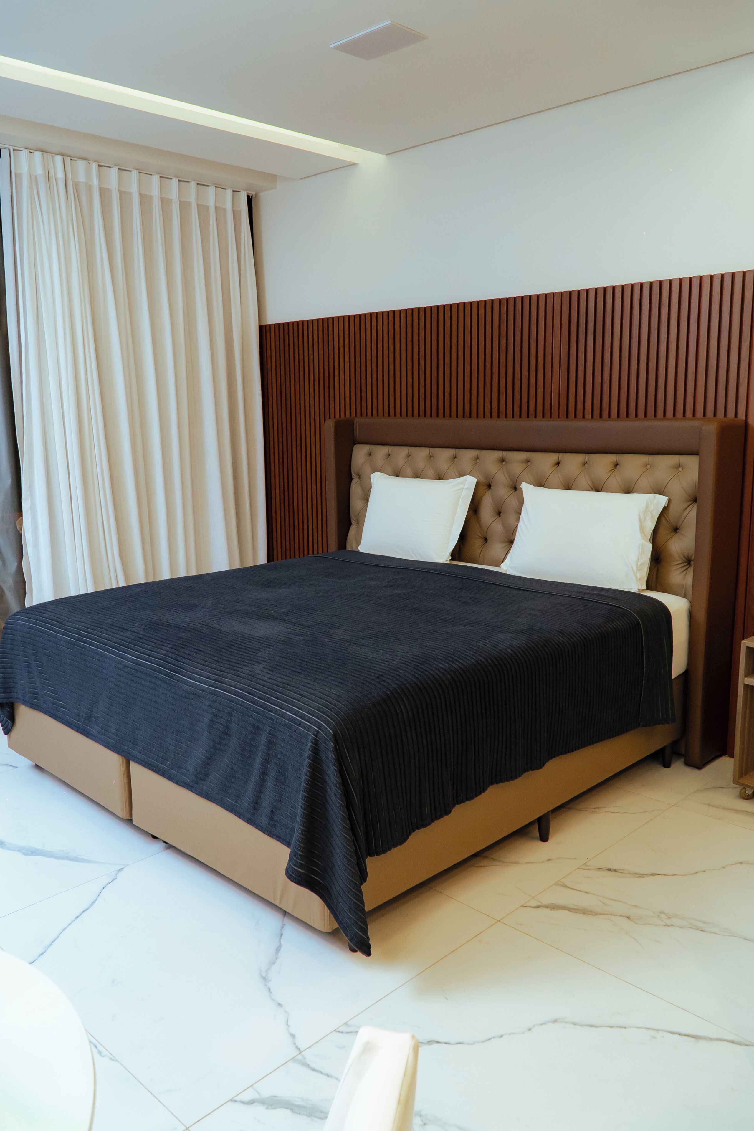 A modern bedroom with a large bed, a wooden headboard, and a marble floor.