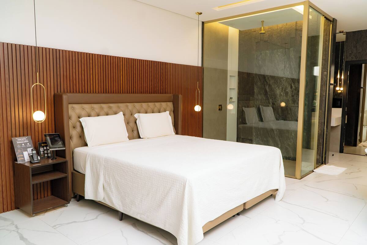 Une chambre moderne avec un grand lit, un mur revêtu de panneaux en bois, des tables de chevet et une cabine de douche en verre.