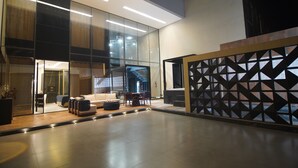 Un interior moderno con un separador de vidrio, una zona de estar con sofá y sillones, y una escalera al fondo.