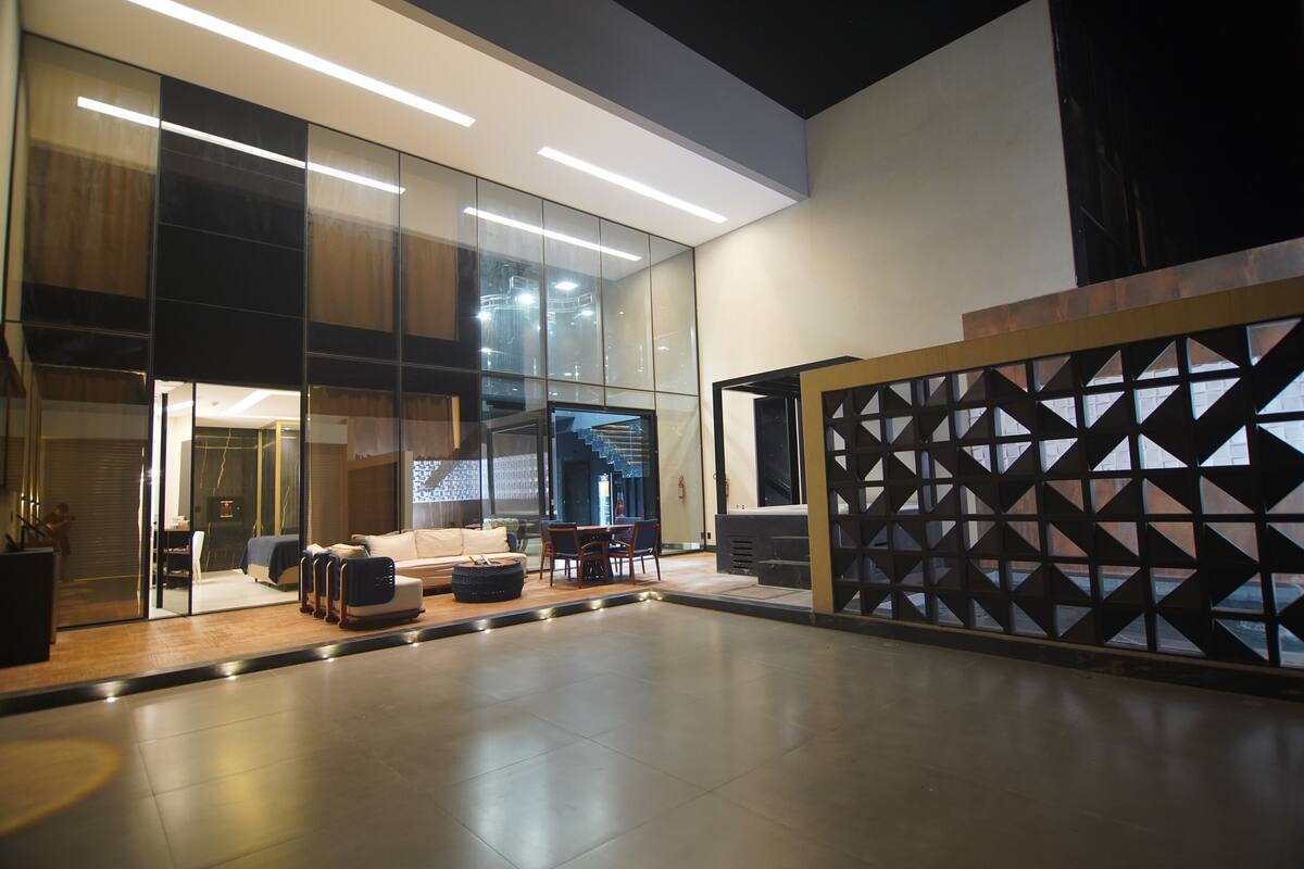 Un intérieur moderne avec une cloison en verre, un coin salon avec un canapé et des fauteuils, et un escalier en arrière-plan.