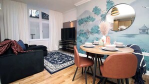 Una sala de estar moderna con un sofá, una mesa de comedor, sillas, un televisor y un mural.