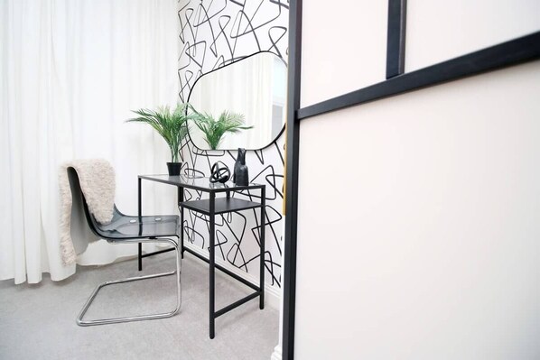 A modern room with a black metal desk, a chair, a small potted plant, and a mirror on the wall.