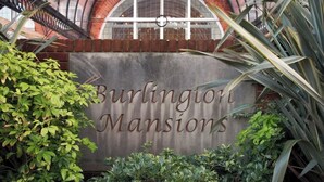 Un letrero de Burlington Mansions, con un arco de ladrillo y follaje en primer plano.