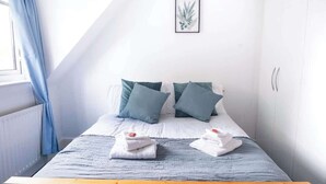 A bedroom with a bed, pillows, a framed picture on the wall, and a window with curtains. - Boho Flat, Sleeps 8, Near Beach Ideal For Groups (Bournemouth)