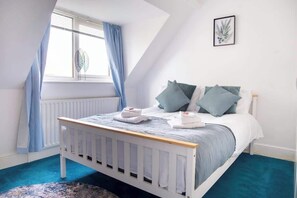 A bedroom with a white crib, a bed with blue bedding, a radiator, and a window with blue curtains.