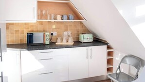 A kitchen with white cabinets, a black countertop, a toaster, a kettle, and a chair. - Boho Flat, Sleeps 8, Near Beach Ideal For Groups (Bournemouth)