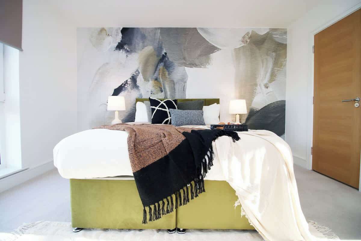 Une chambre à coucher avec un lit, deux lampes de chevet, un grand tableau abstrait accroché au mur et une porte en bois.