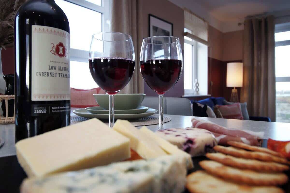 A hotel room with a table set for a meal, featuring cheese, crackers, and wine glasses.