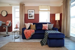 A living room with a blue sofa, a small round table, a lamp, and a clock on the wall.