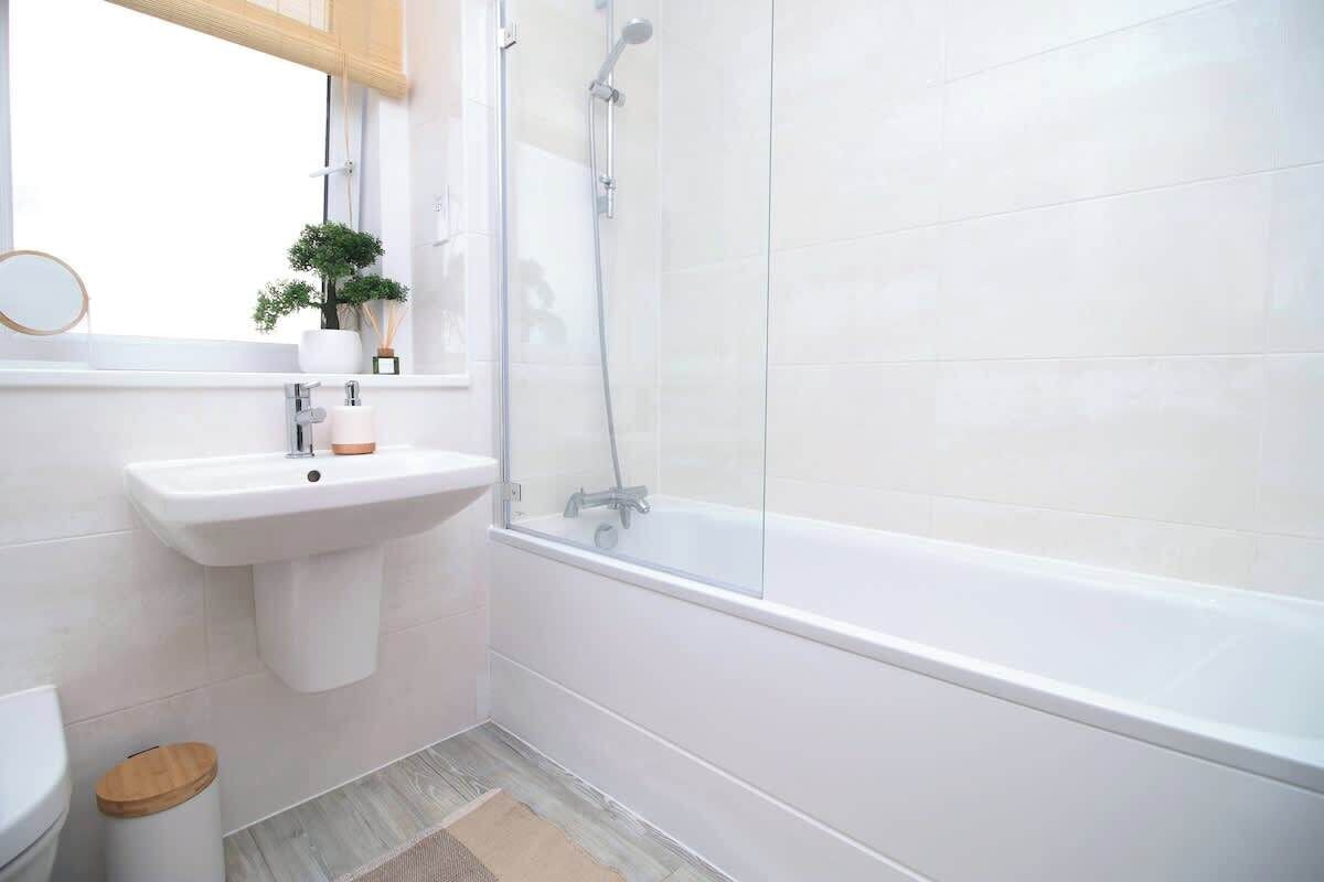 Une salle de bain avec un lavabo blanc, des toilettes, un bidet, une douche et un petit tabouret en bois.