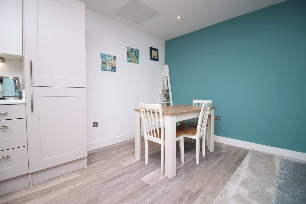 A compact kitchen with white cabinetry, a dining table with chairs, teal walls, and a herringbone-patterned floor.