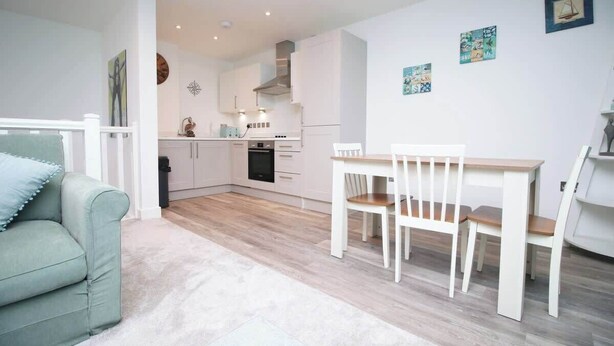 Una cocina moderna con armarios blancos, una mesa de comedor con sillas y un sofá de tonos claros.