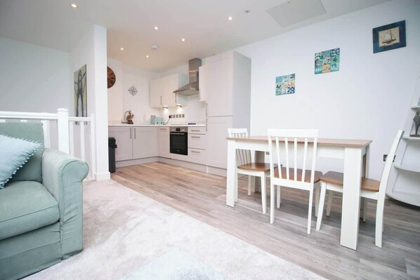 A modern kitchen with white cabinets, a dining table with chairs, and a light-colored sofa.