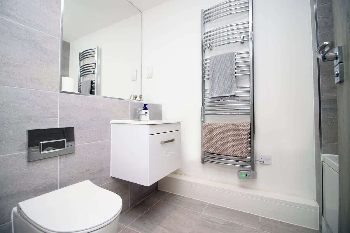 Ein modernes Badezimmer mit Toilette, Waschbecken mit Spiegel, Handtuchhalter und Duschbereich.