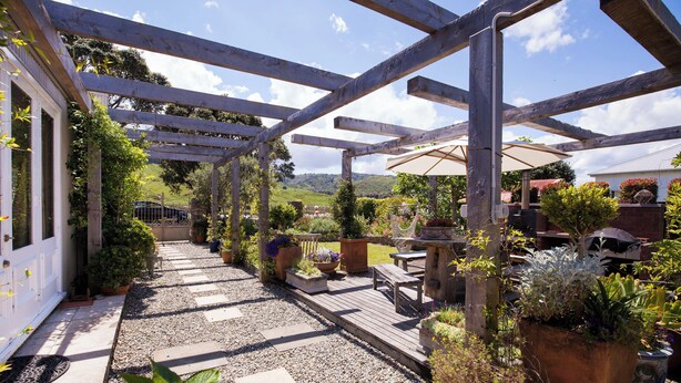 A wooden pergola structure with a gravel pathway and potted plants.
