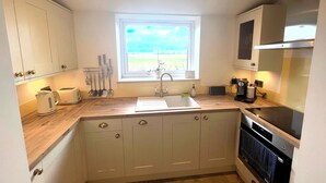A compact kitchen with white cabinets, a window with a view, a sink, a toaster, and an oven. - Small 3 bedroom converted stable in Norfolk (Upton)