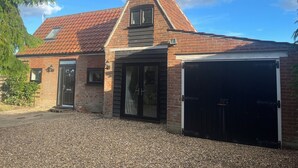 A two-story house with a red-tiled roof, a brick facade, and a garage. - Small 3 bedroom converted stable in Norfolk (Upton)