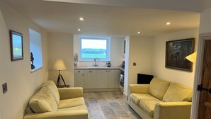 A compact living space with two sofas, a dining area, a window with a view, and a painting on the wall. - Small 3 bedroom converted stable in Norfolk (Upton)
