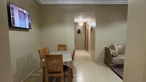 A hallway with a dining area featuring a table and chairs, a television mounted on the wall, and a ceiling light fixture. - Accommodation 20 minutes from Marrakech (Chwiter)