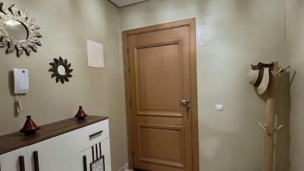 A hallway with a wooden door, a white cabinet with decorative items, a wall-mounted mirror, and a ceiling light fixture. - Accommodation 20 minutes from Marrakech (Chwiter)
